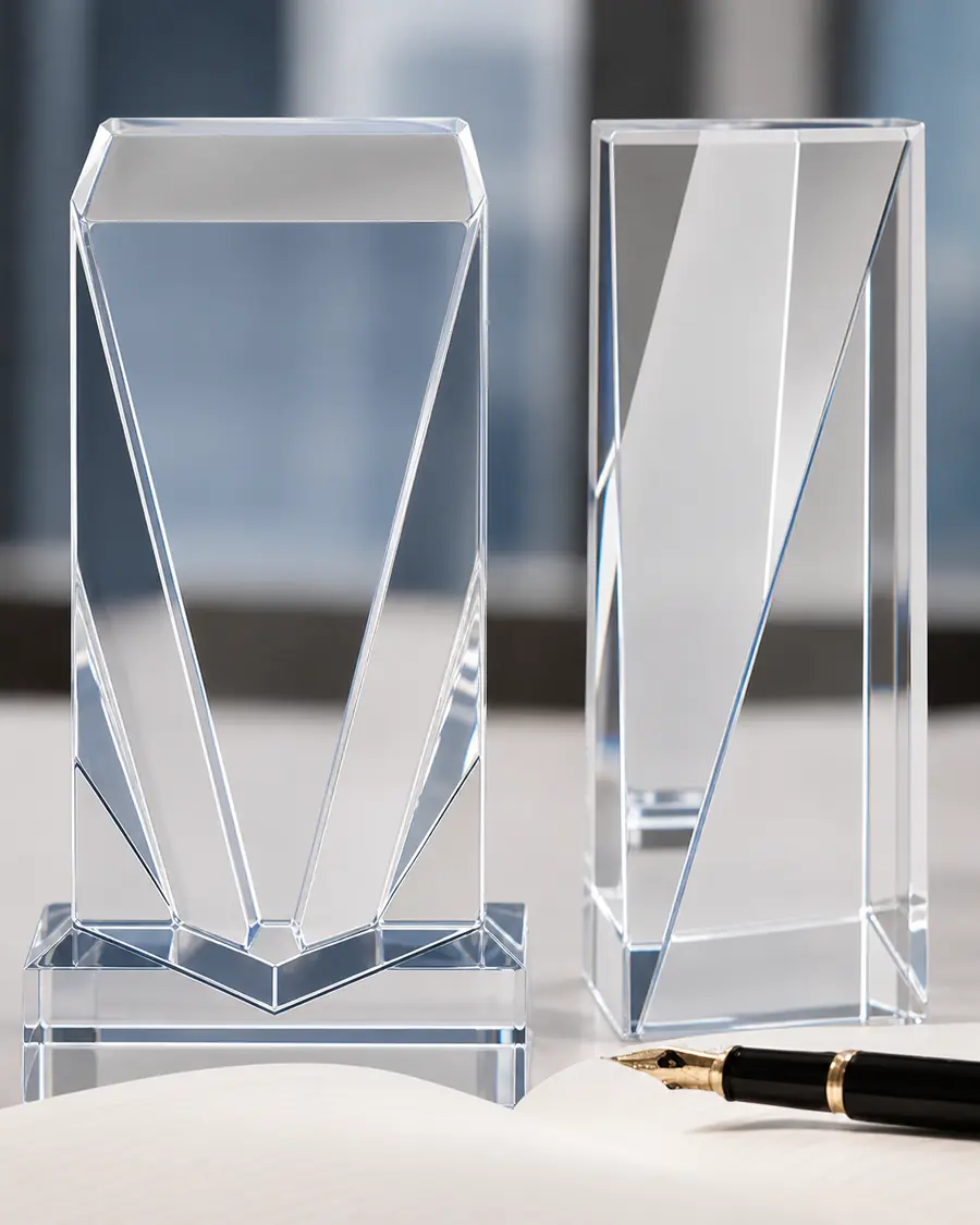Two clear faceted column awards on square bases, standing on a desk beside a fountain pen