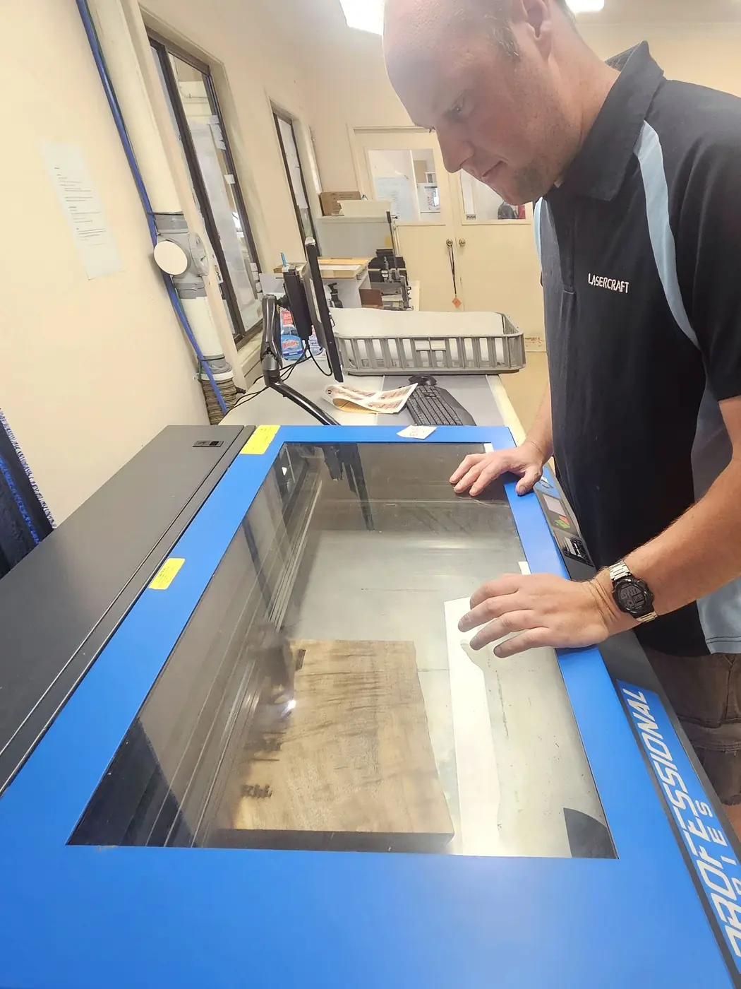 A team member with both hands on the open bed of the laser cutter in the West Gosford workshop, checking the work.