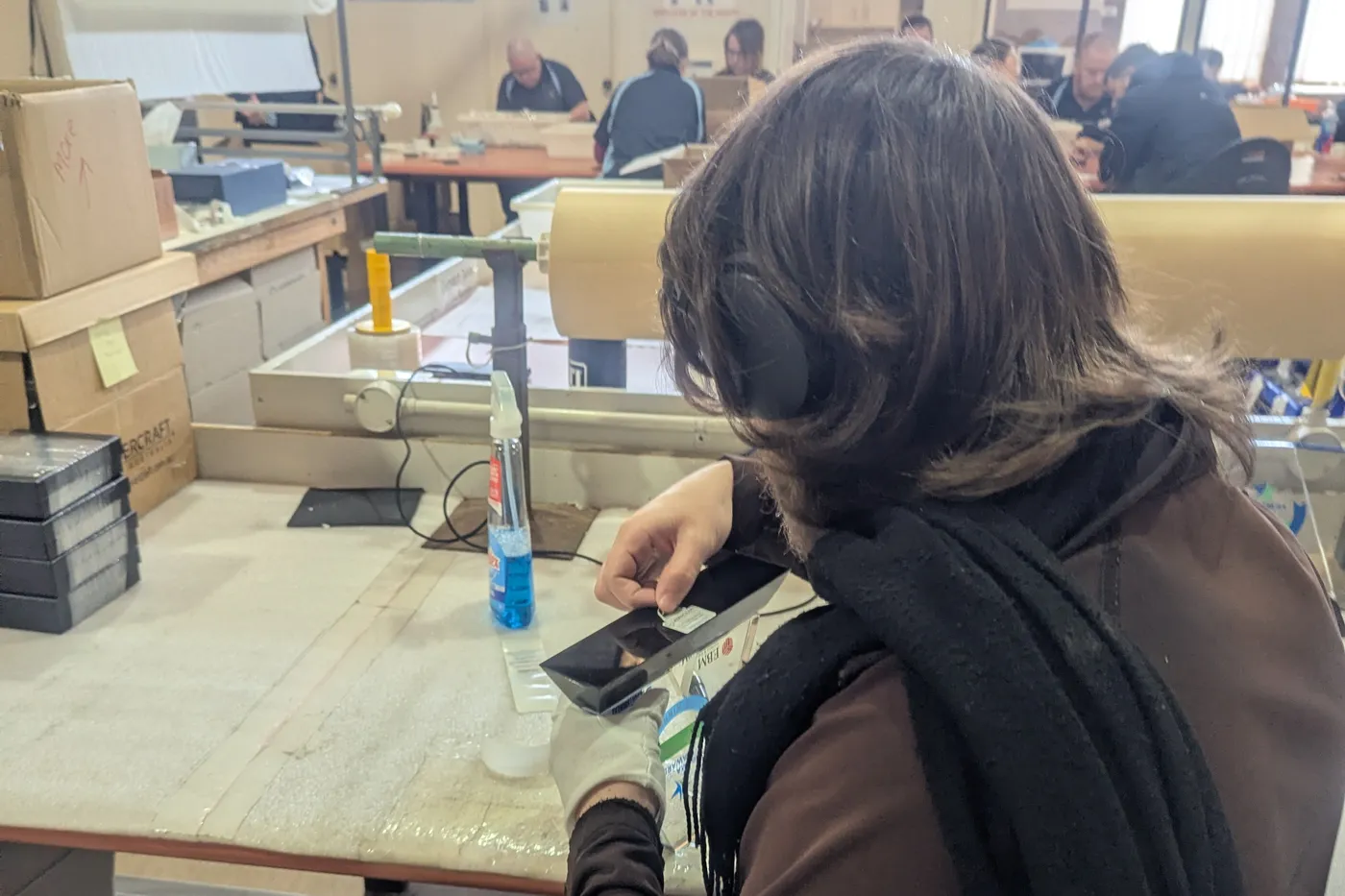 A team member in ear protection working at a long packing bench on the production floor at West Gosford, with more of the team at benches behind.